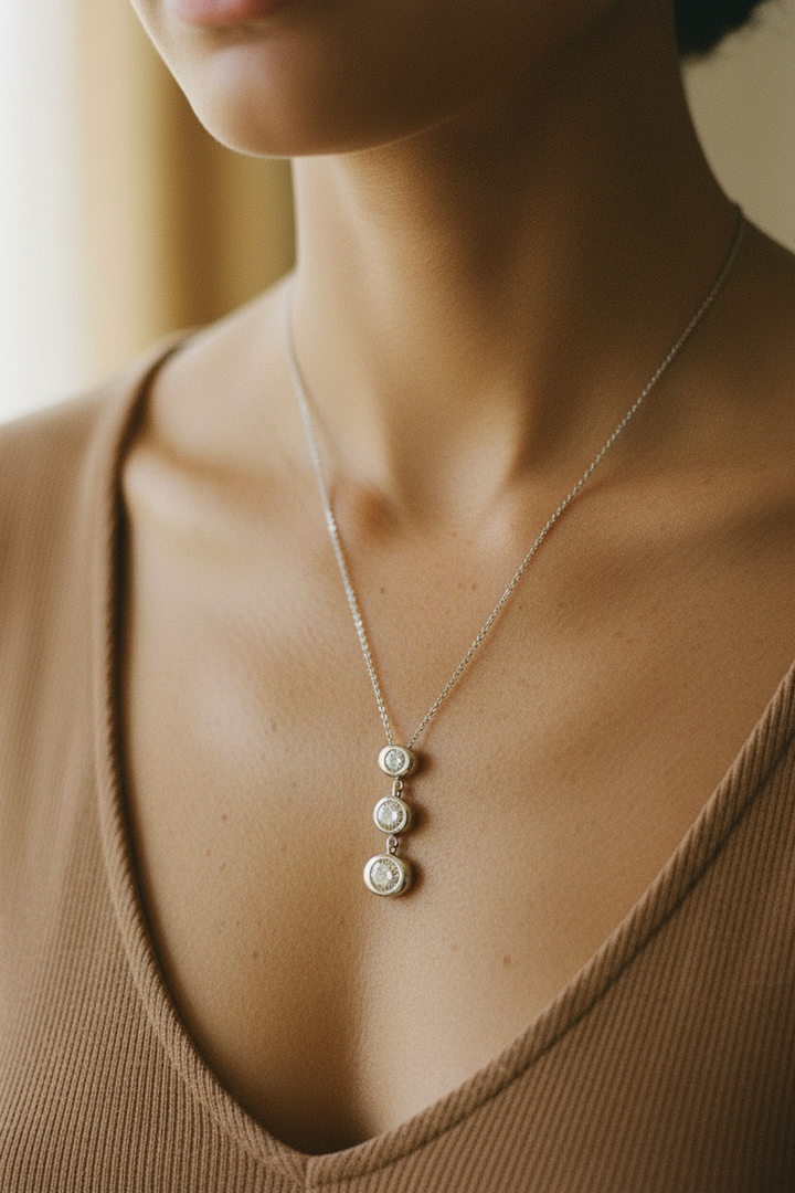 Necklace with three circular pendants on a person wearing a brown top.