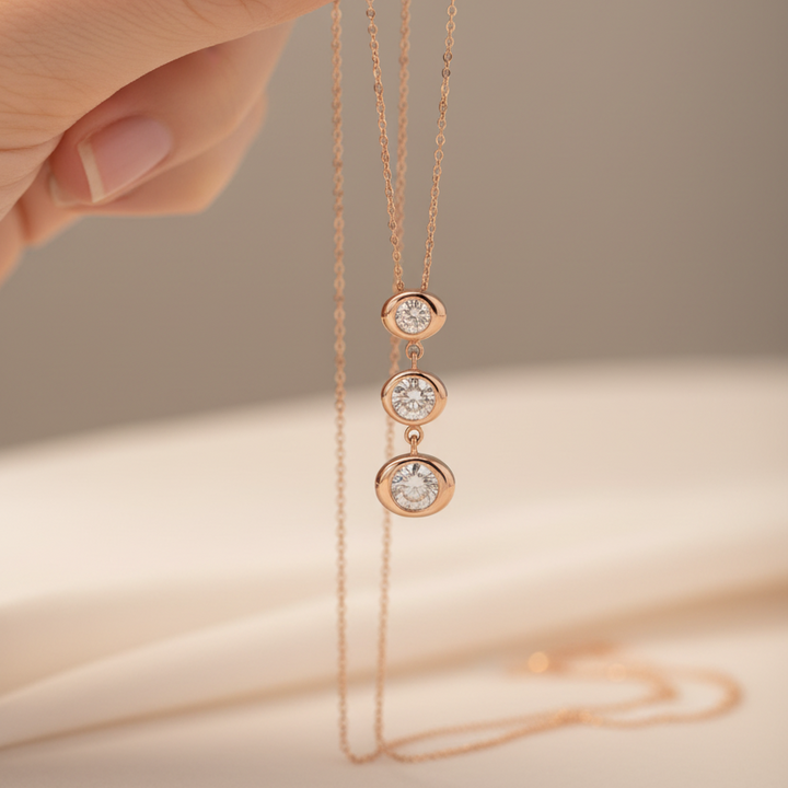 Rose gold necklace with three diamond pendants held by a hand against a beige background